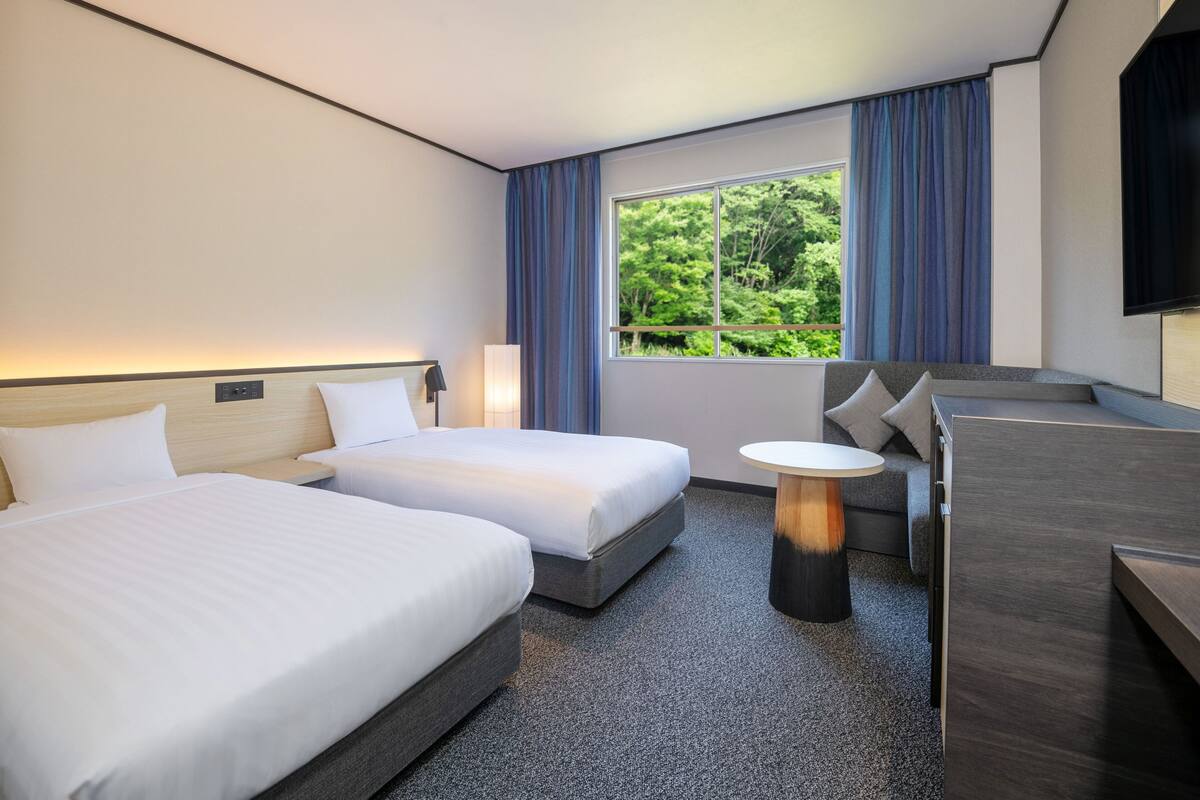 Ein modernes Hotelzimmer mit zwei Betten, einem kleinen Tisch, einer Couch und einem Fernseher.