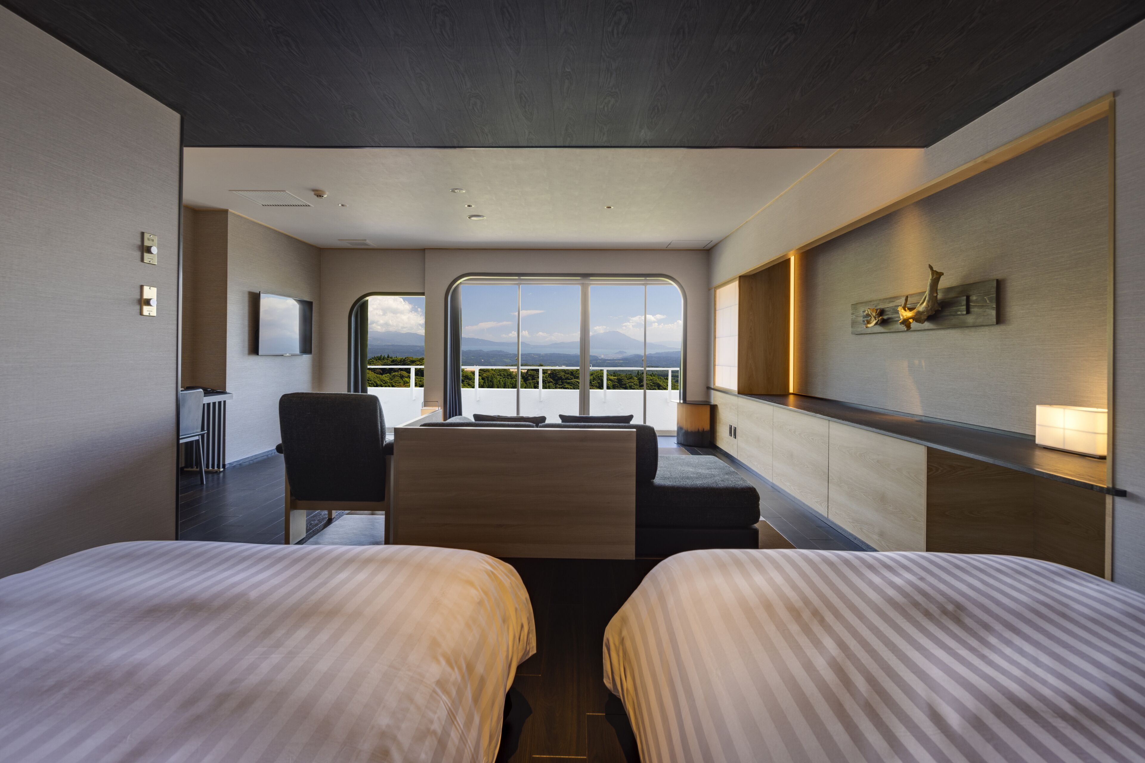 A modern hotel room with two beds, a desk, and a large window offering a view of the mountains.