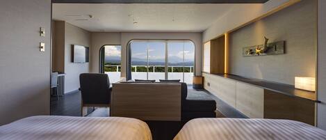 A modern hotel room with two beds, a desk, and a large window offering a view of the mountains.
