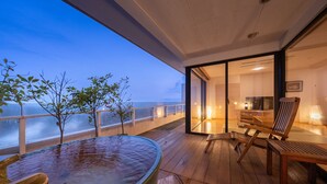 Een houten terras met een jacuzzi, stoelen en uitzicht op de oceaan in de schemering.