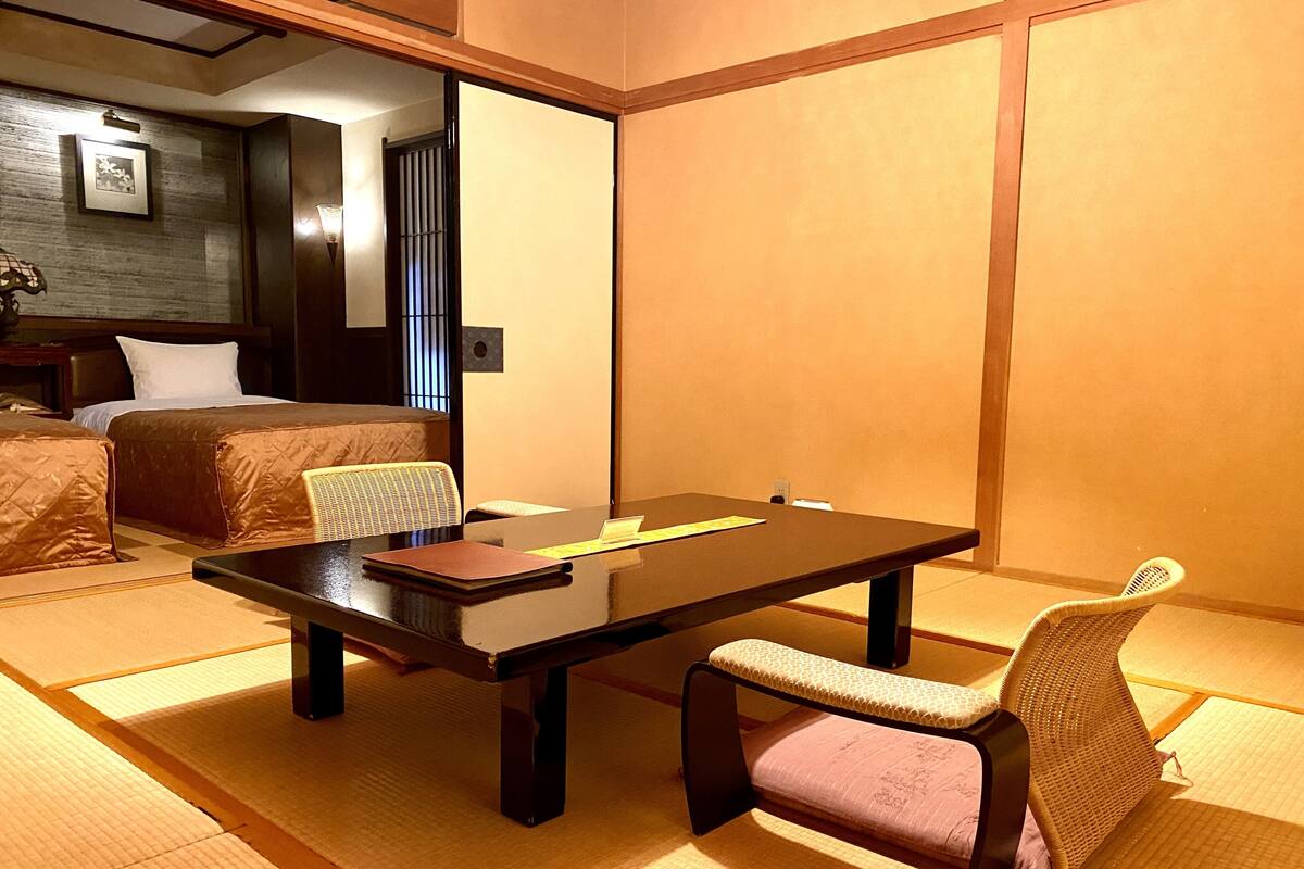 A traditional Japanese-style room with tatami flooring, a low table, and a bed with a headboard.