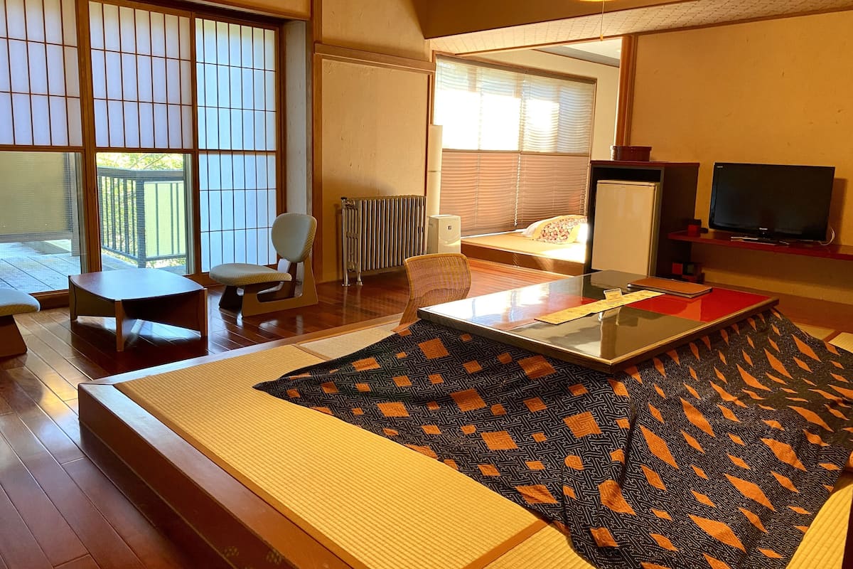 A hotel room with a sofa, a small table, a chair, a TV, and a large window with blinds.