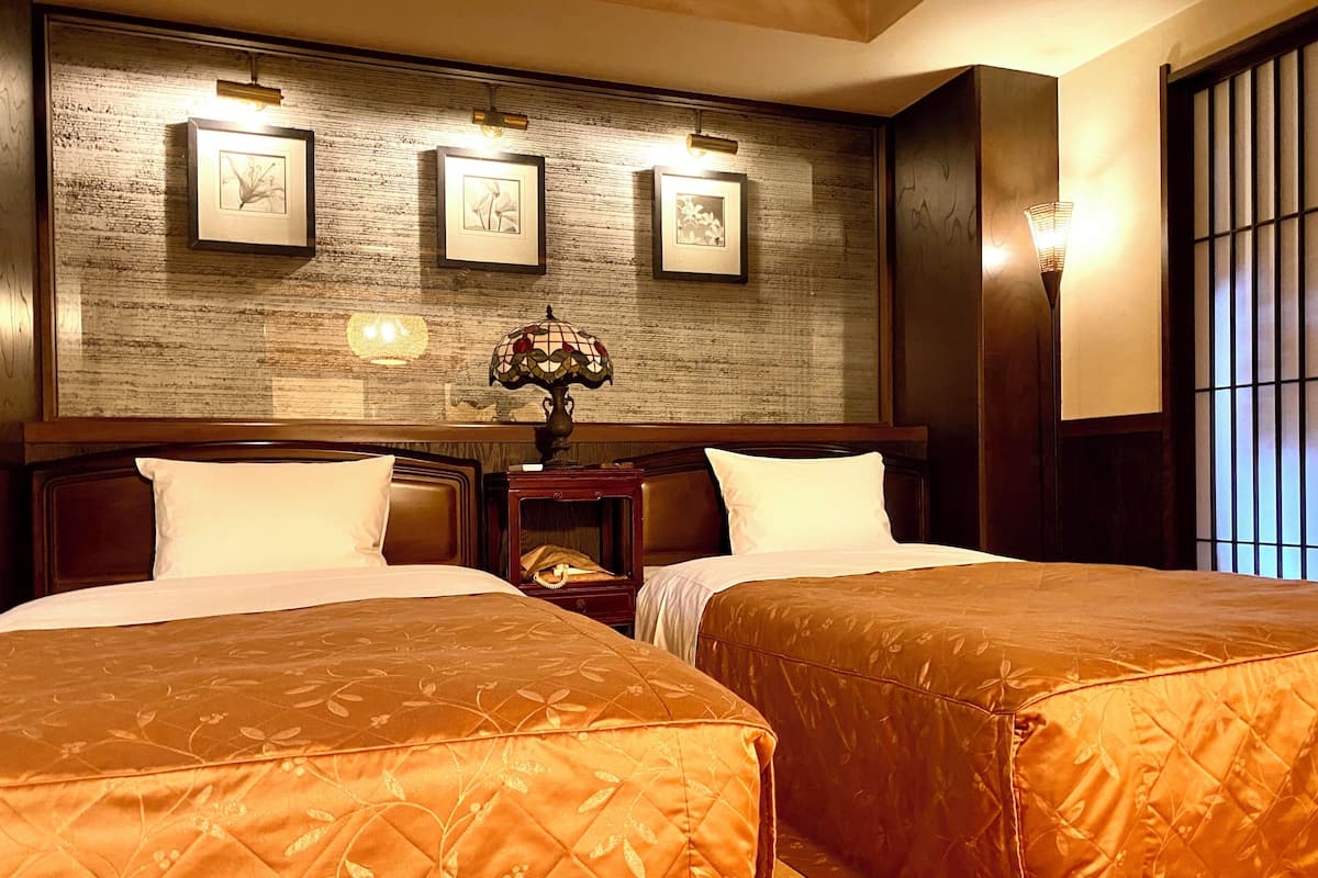 A hotel room with two beds, a wooden headboard, framed artwork on the wall, and a nightstand with a lamp.