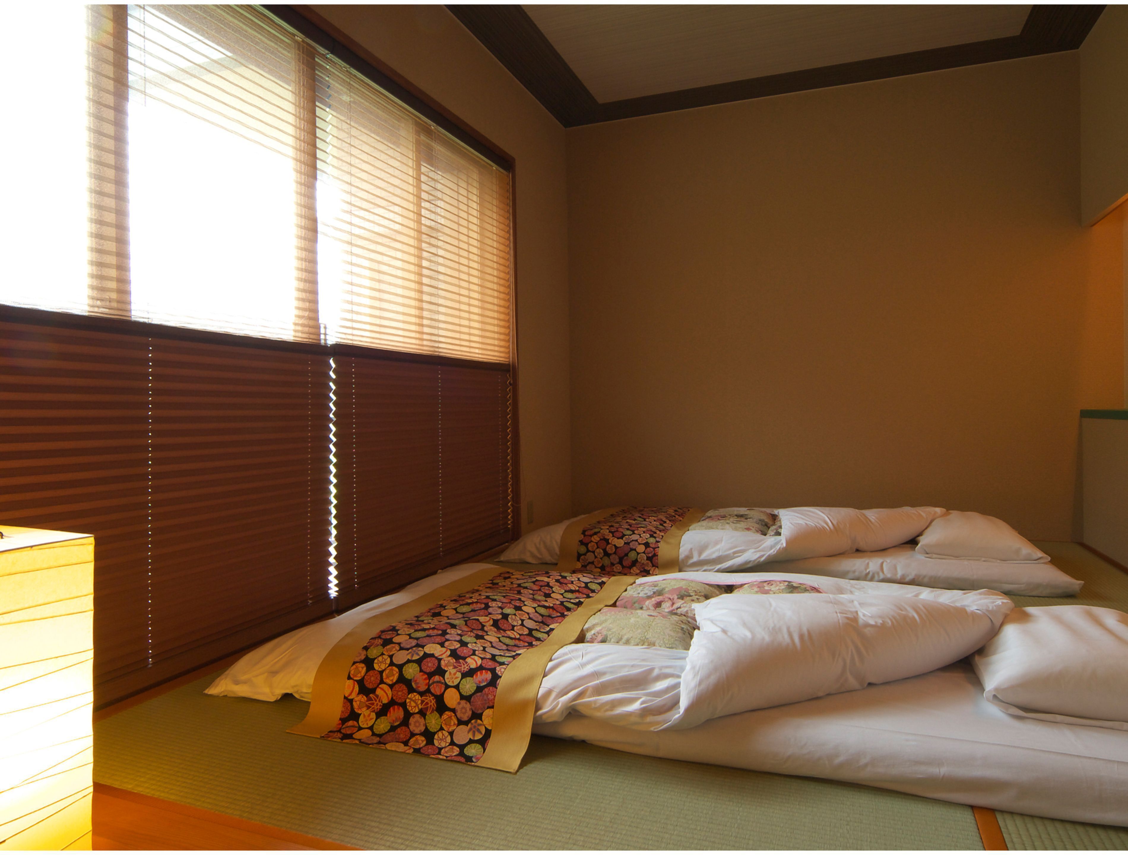 A room with two beds, a window with blinds, and a lamp.