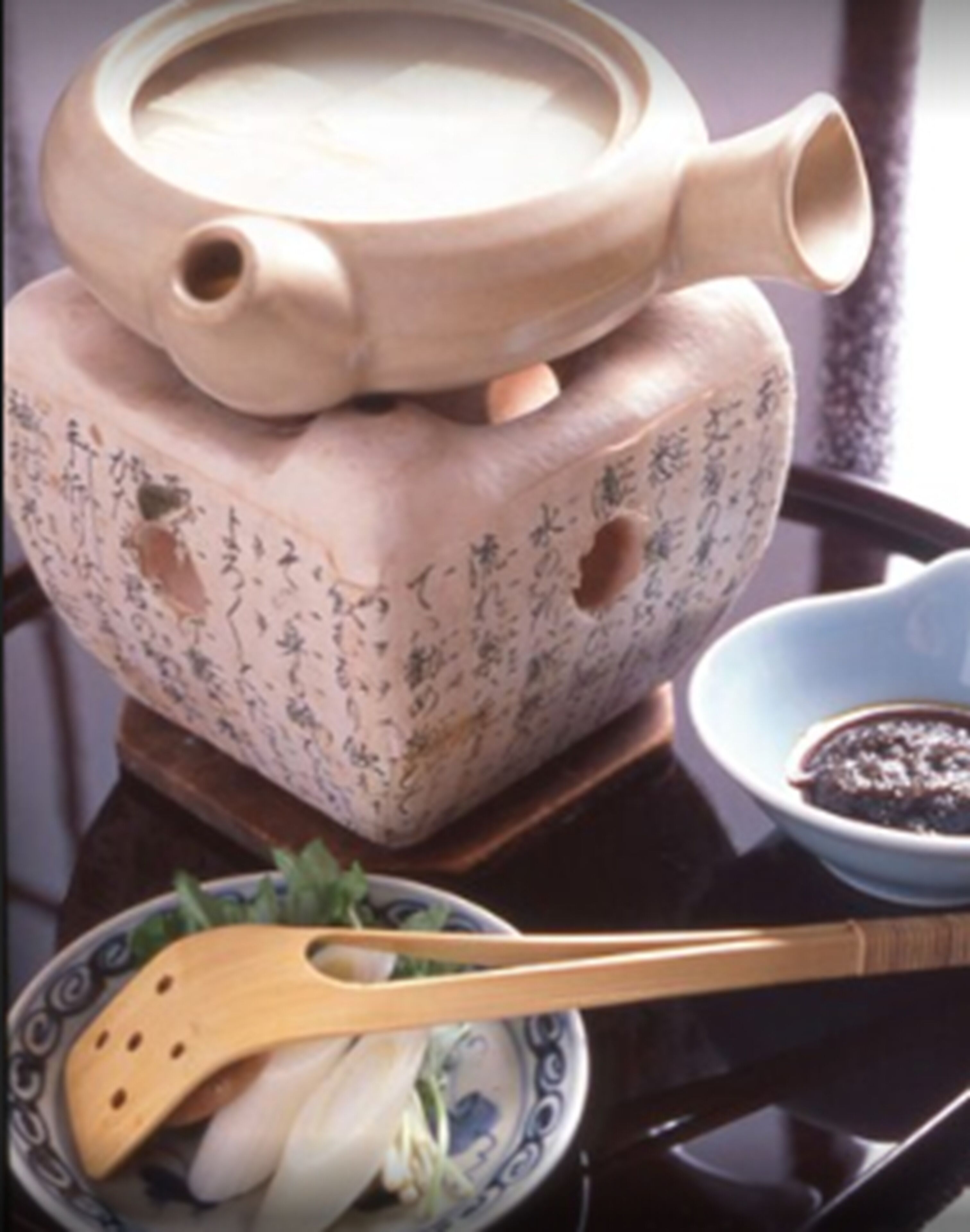 A traditional tea set with a teapot and cups, a bowl of tea, and a wooden spoon.