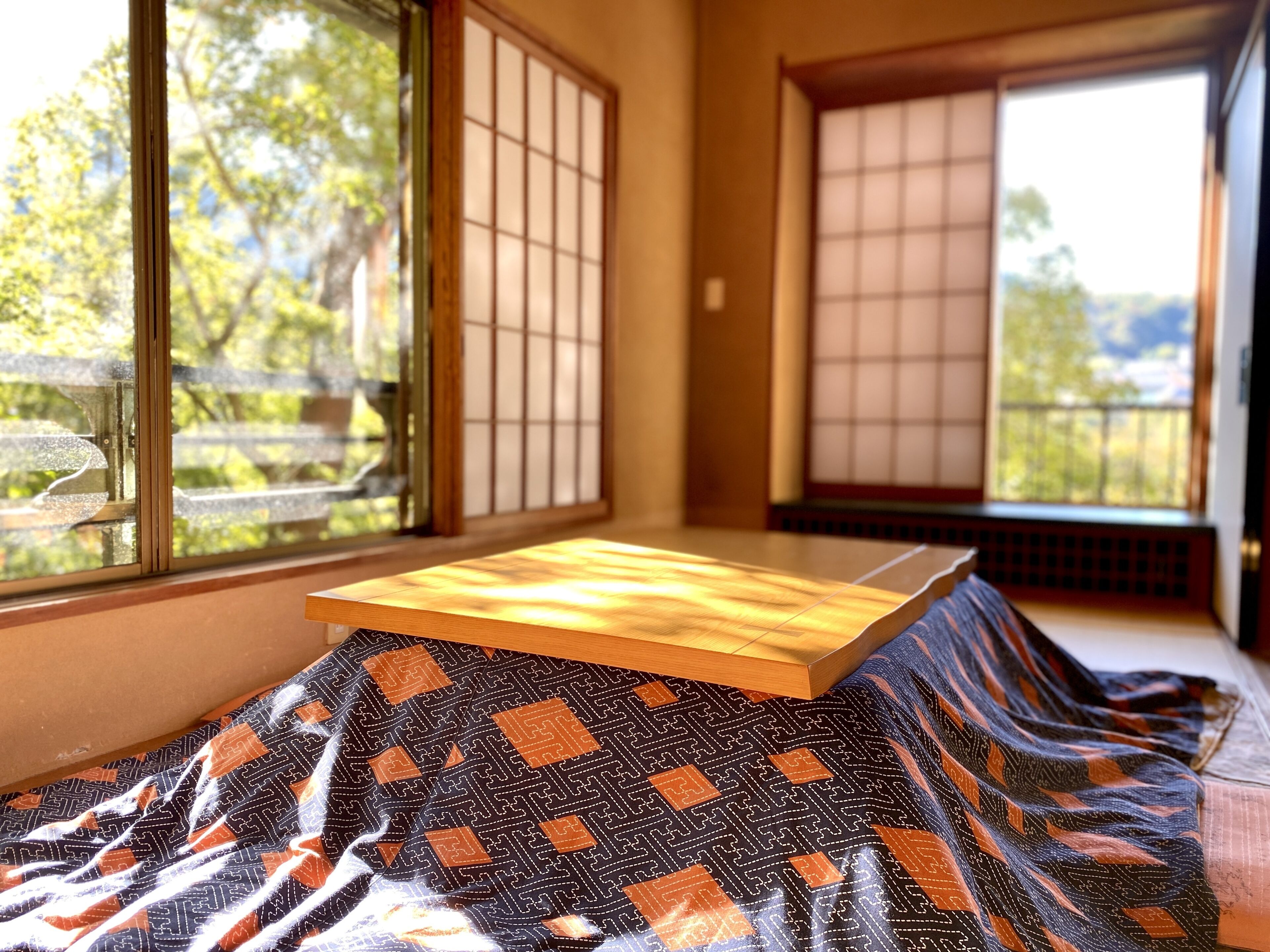 Ein Raum mit Tatami-Matten, einem niedrigen Holztisch und Blick auf Bäume durch Shoji-Schirme.