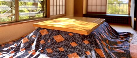 Ein Raum mit Tatami-Matten, einem niedrigen Holztisch und Blick auf Bäume durch Shoji-Schirme.