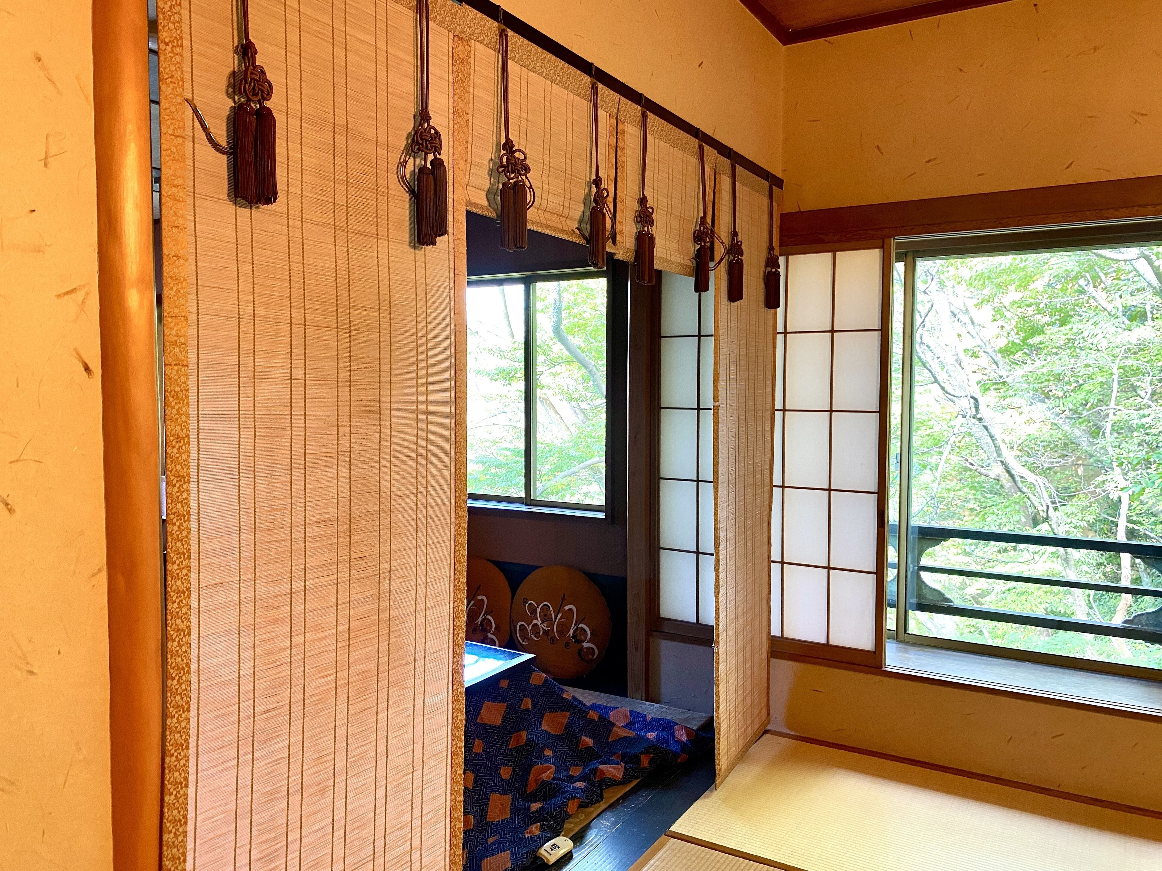 A traditional Japanese room with tatami flooring, shoji screens, and a view of trees outside.