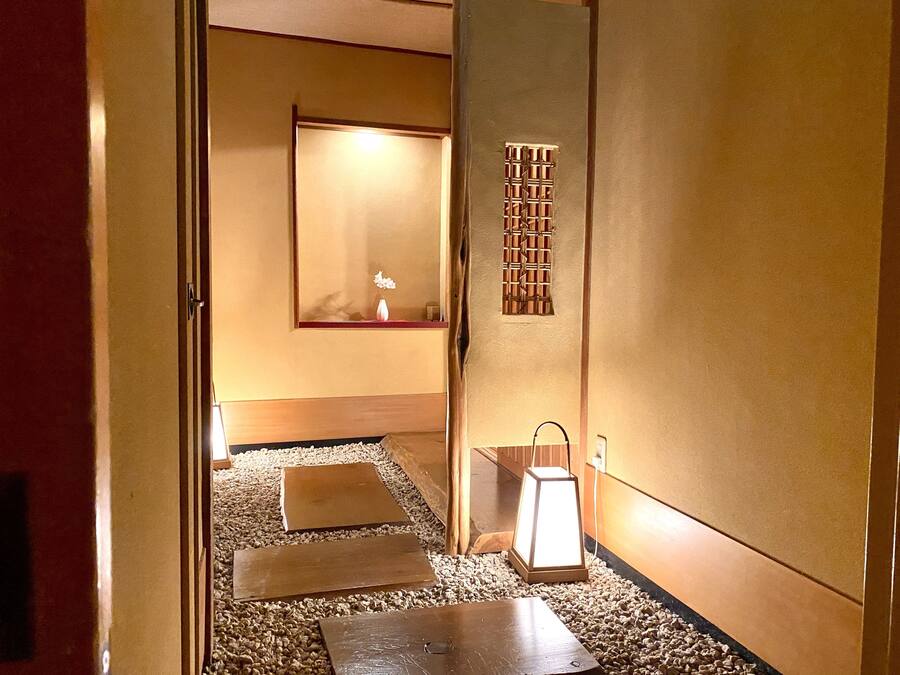 Ein Flur mit Holzboden, einem kleinen Tisch, einer Laterne und einem an der Wand befestigten Regal mit Spiegel und kleiner Vase.