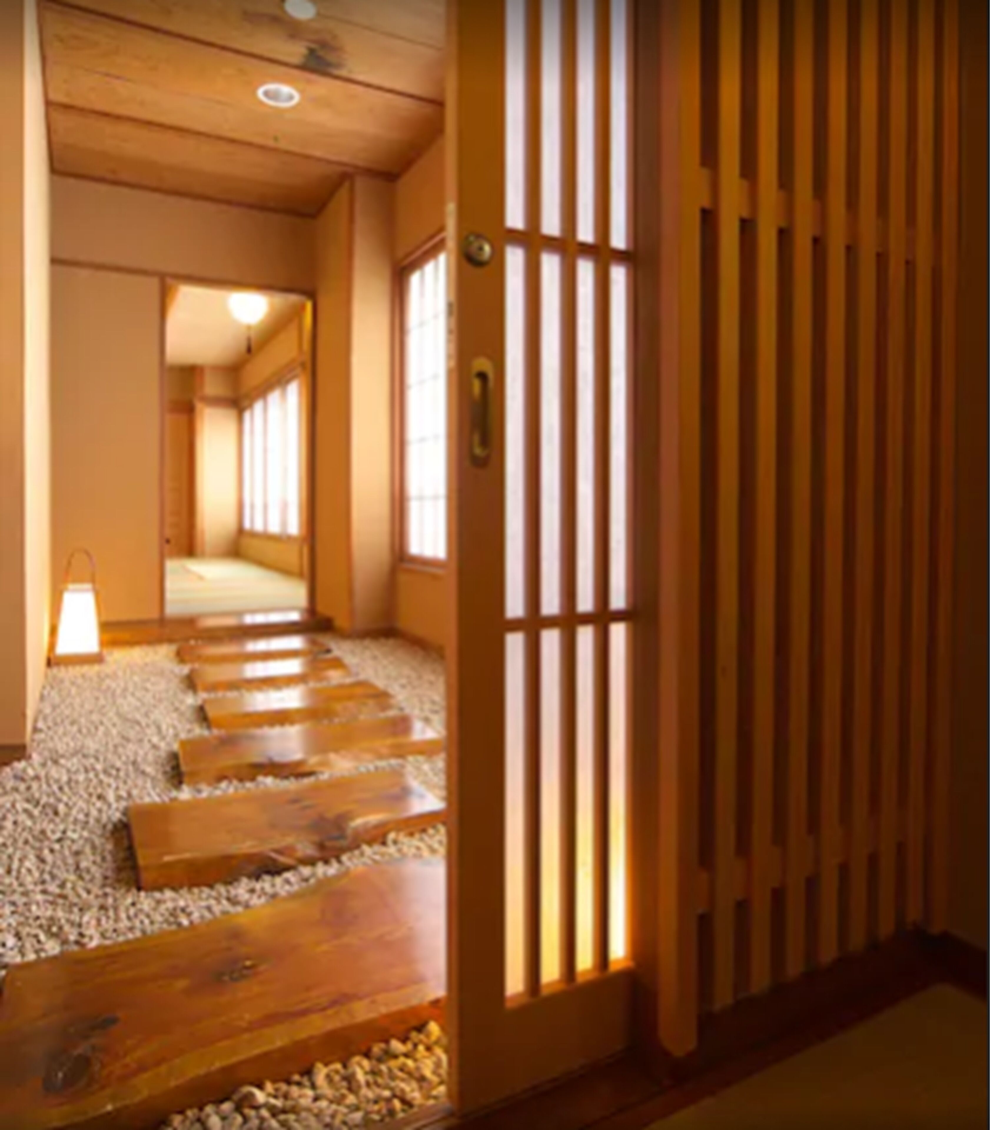 A traditional Japanese interior with a wooden floor leading to a room, a sliding door with vertical slats, and a small lantern on the left.