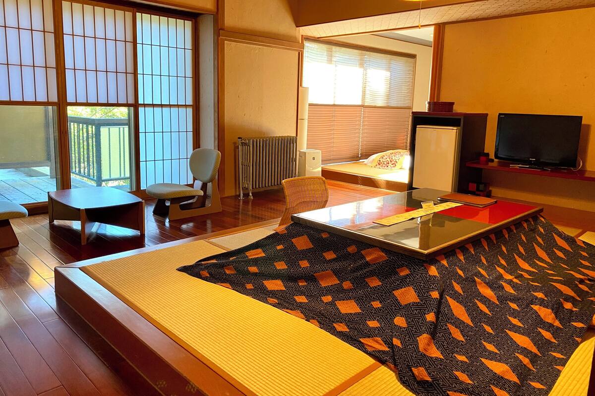A hotel room with a sofa, a small table, a chair, a TV, and a large window with blinds.