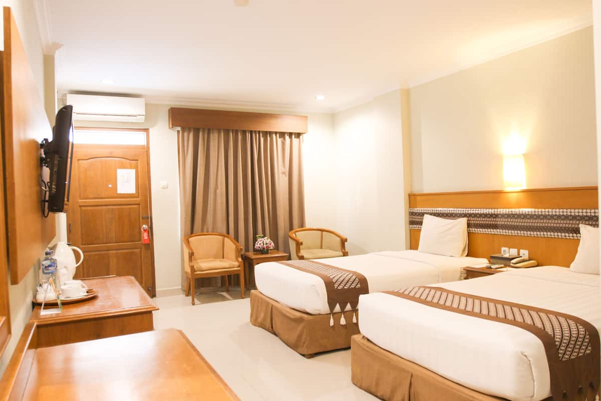 A hotel room with two beds, a desk with a coffee maker, a TV, and a window with curtains.