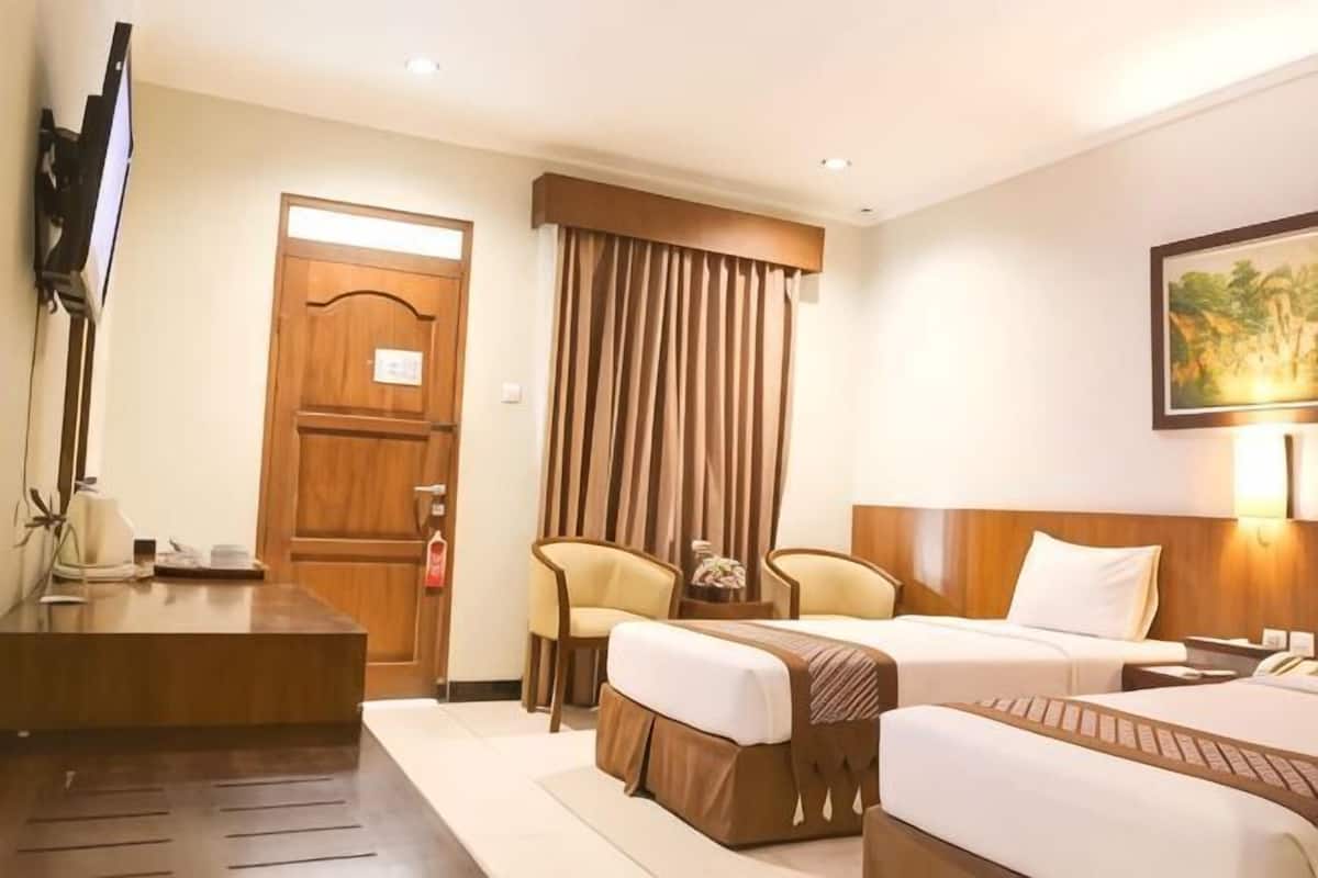 A hotel room with two beds, a desk, a TV, and a large window with curtains.