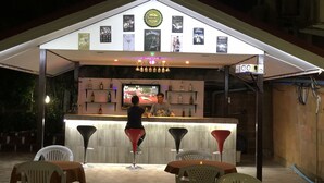 Un área de bar al aire libre con mostrador, taburetes y una pantalla de televisión.
