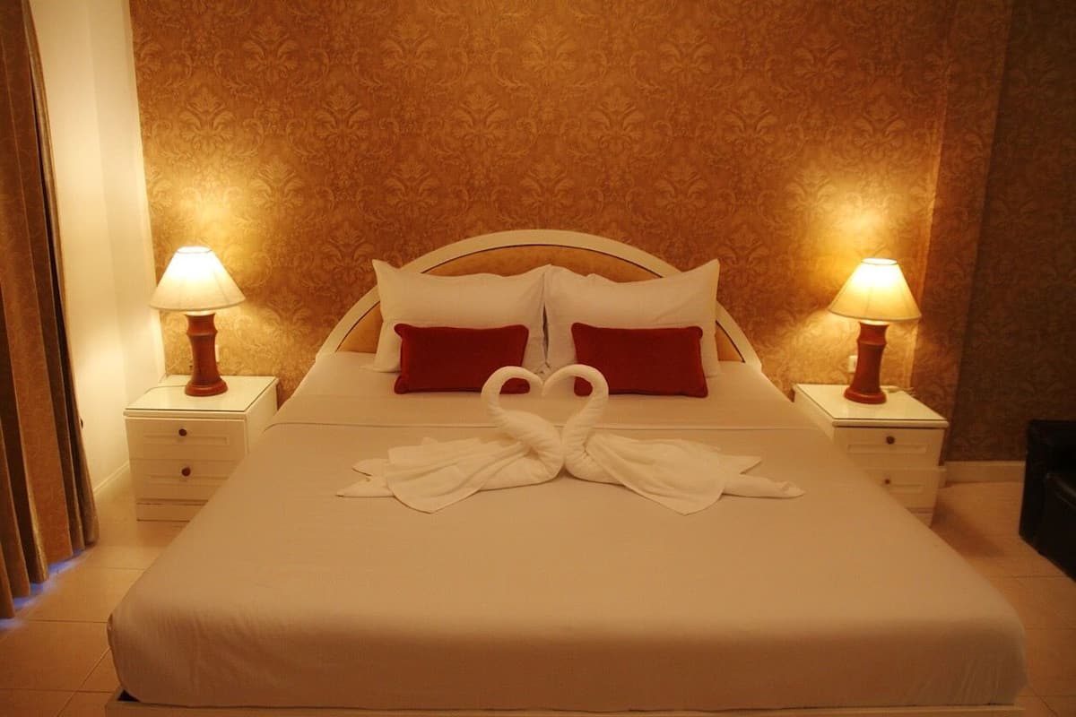A neatly made bed with red pillows, two bedside lamps, and a swan-shaped towel arrangement on the bed.