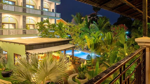 Hotel com piscina, vegetação exuberante e área externa coberta à noite.
