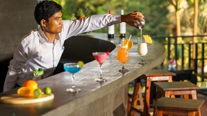 Um bartender preparando bebidas em um bar, com diversos coquetéis e uma guarnição de frutas.