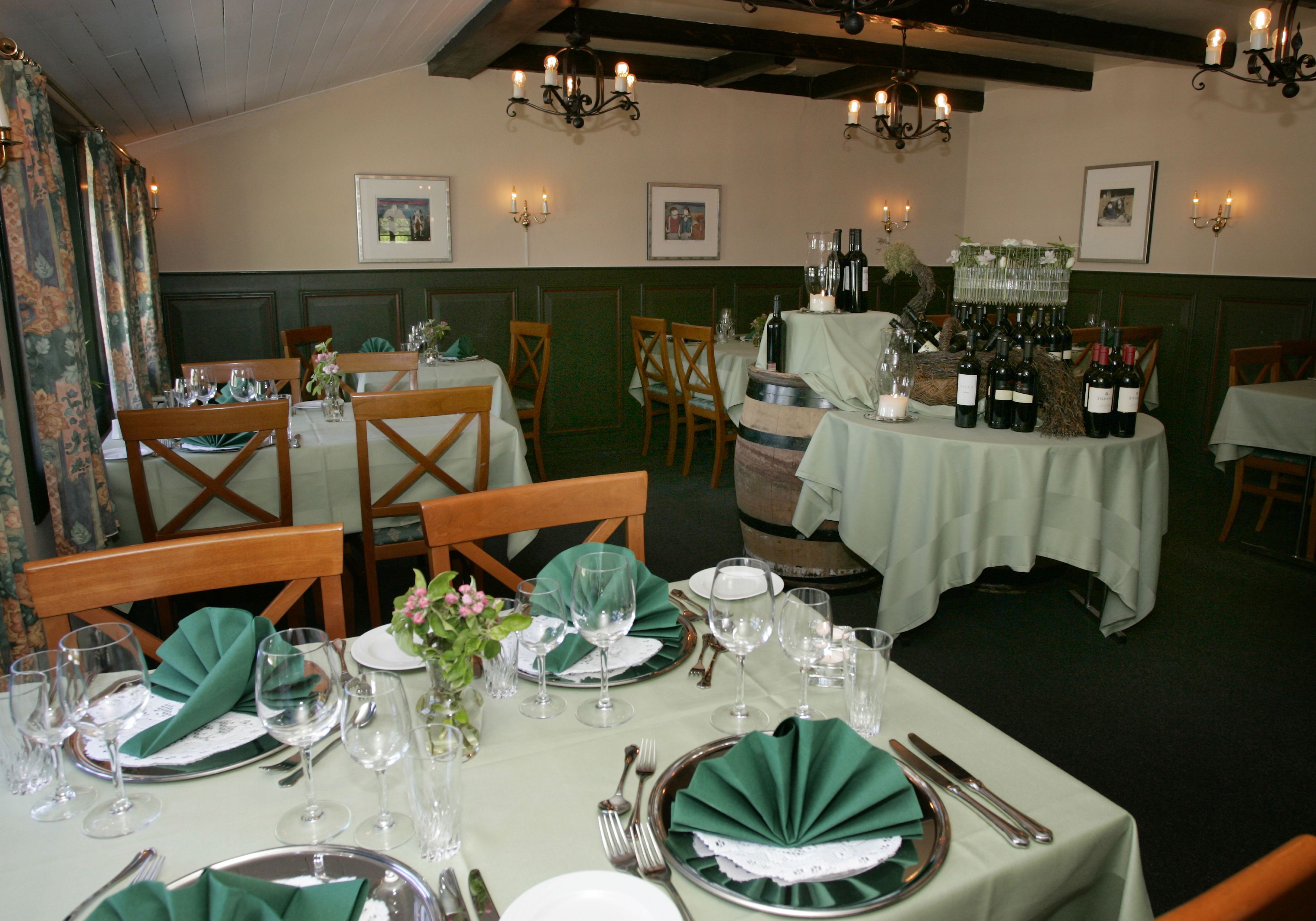 A restaurant interior with tables set for dining, featuring green tablecloths, wine glasses, and bottles.