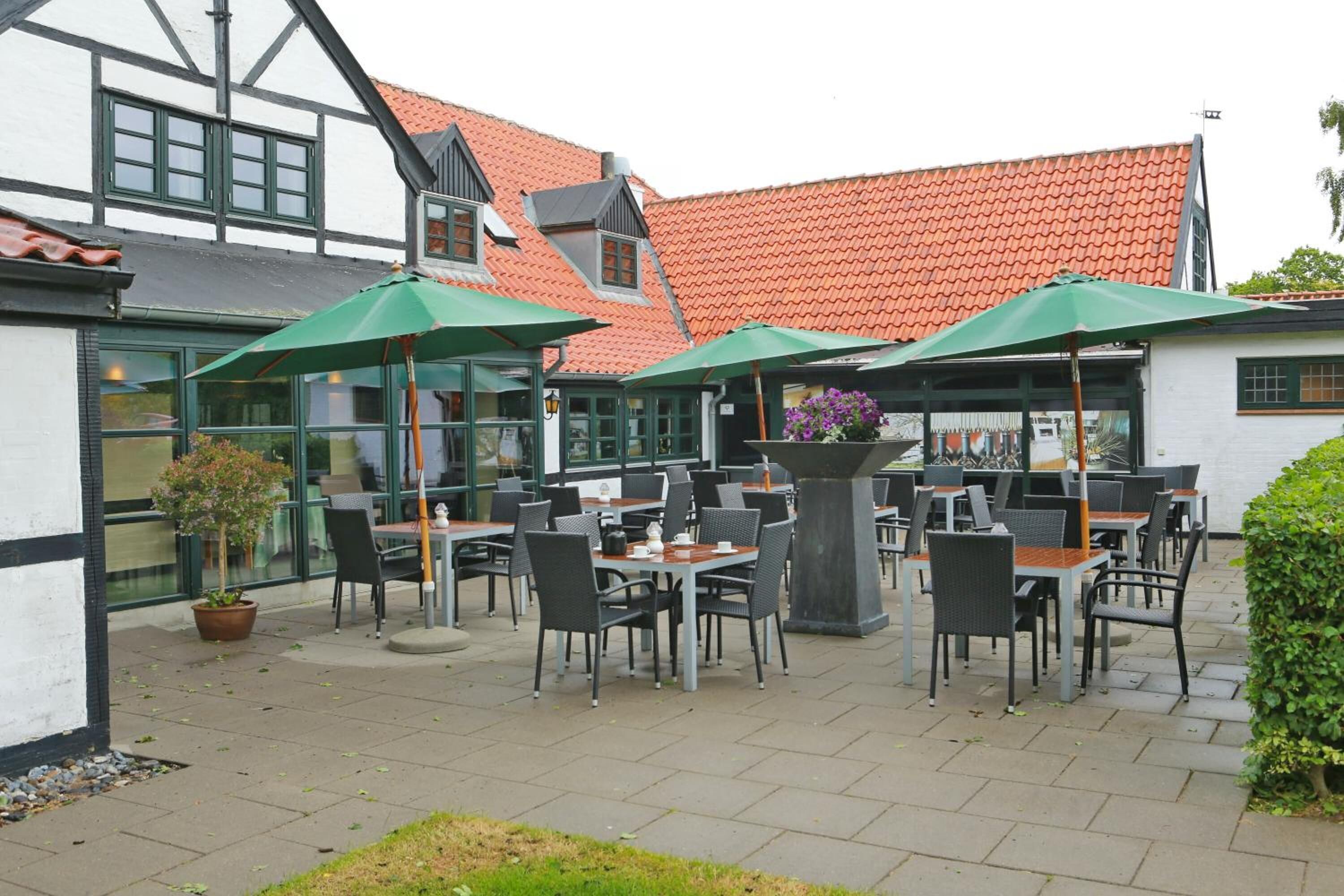 An outdoor cafe with tables and chairs, green umbrellas, and potted plants.
