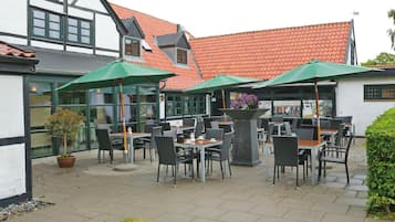 An outdoor cafe with tables and chairs, green umbrellas, and potted plants.