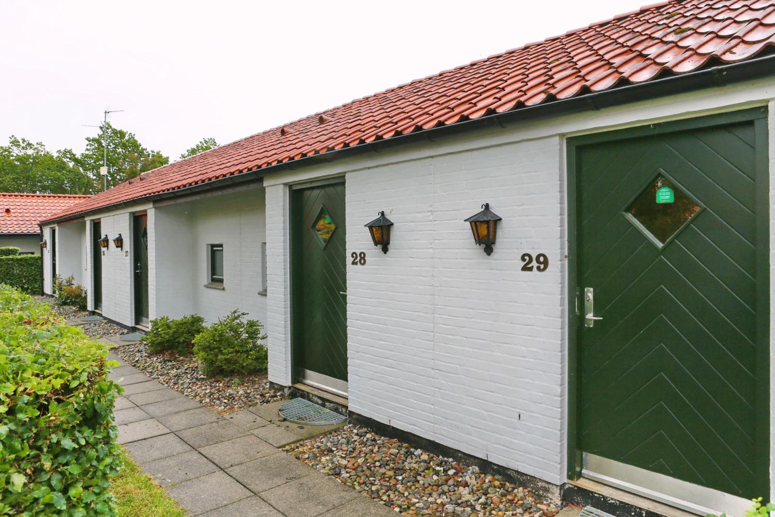A row of white buildings with red-tiled roofs, numbered 28 and 29, featuring green doors and small windows.