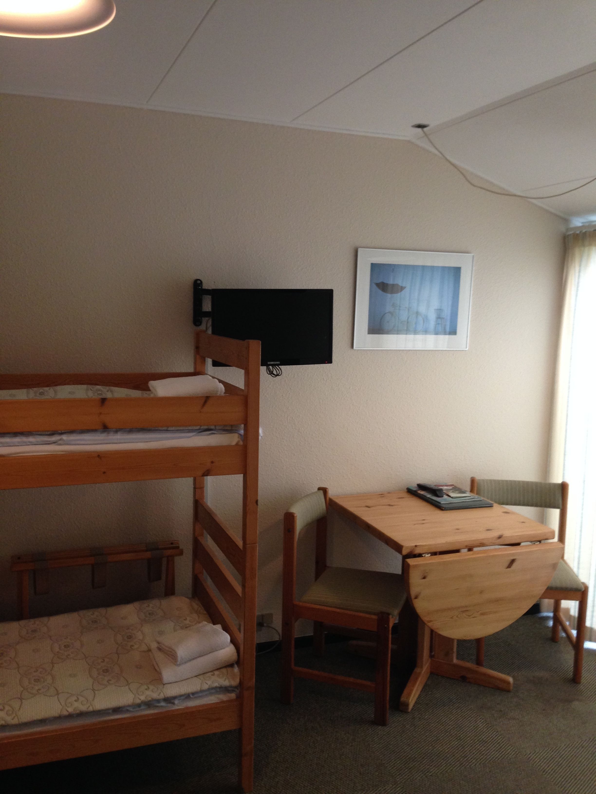 Ein Etagenbett mit an der Wand befestigtem Fernseher, ein Schreibtisch mit Stuhl und ein gerahmtes Bild an der Wand.