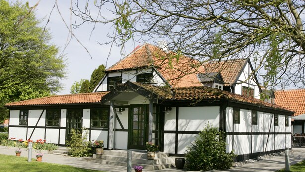 Une maison traditionnelle à colombages, dotée d’un toit à forte pente, d’un porche et d’un jardin bien entretenu.