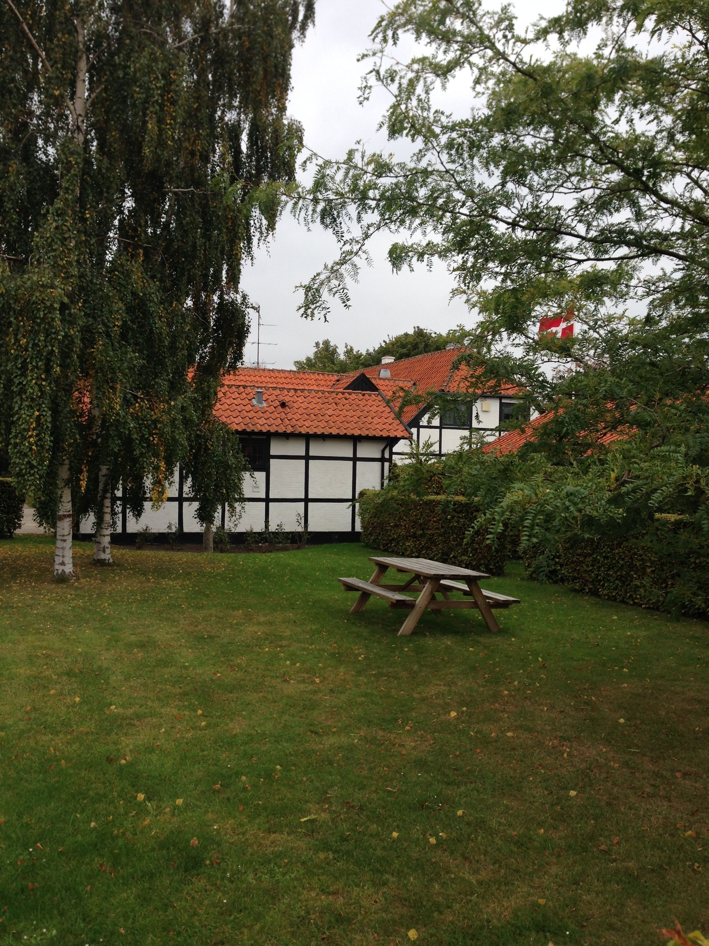En traditionel bygning med et tagdækket tag og hvide vægge, omgivet af en græsplæne med et picnicbord.