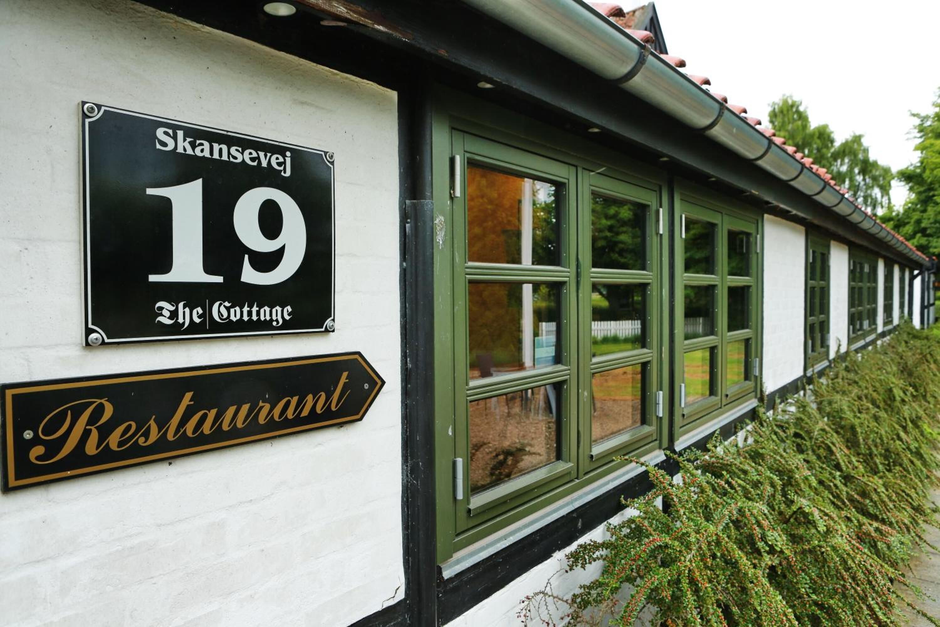 A building with a sign indicating 'Skansevej 19 The Cottage' and a 'Restaurant' sign below it.
