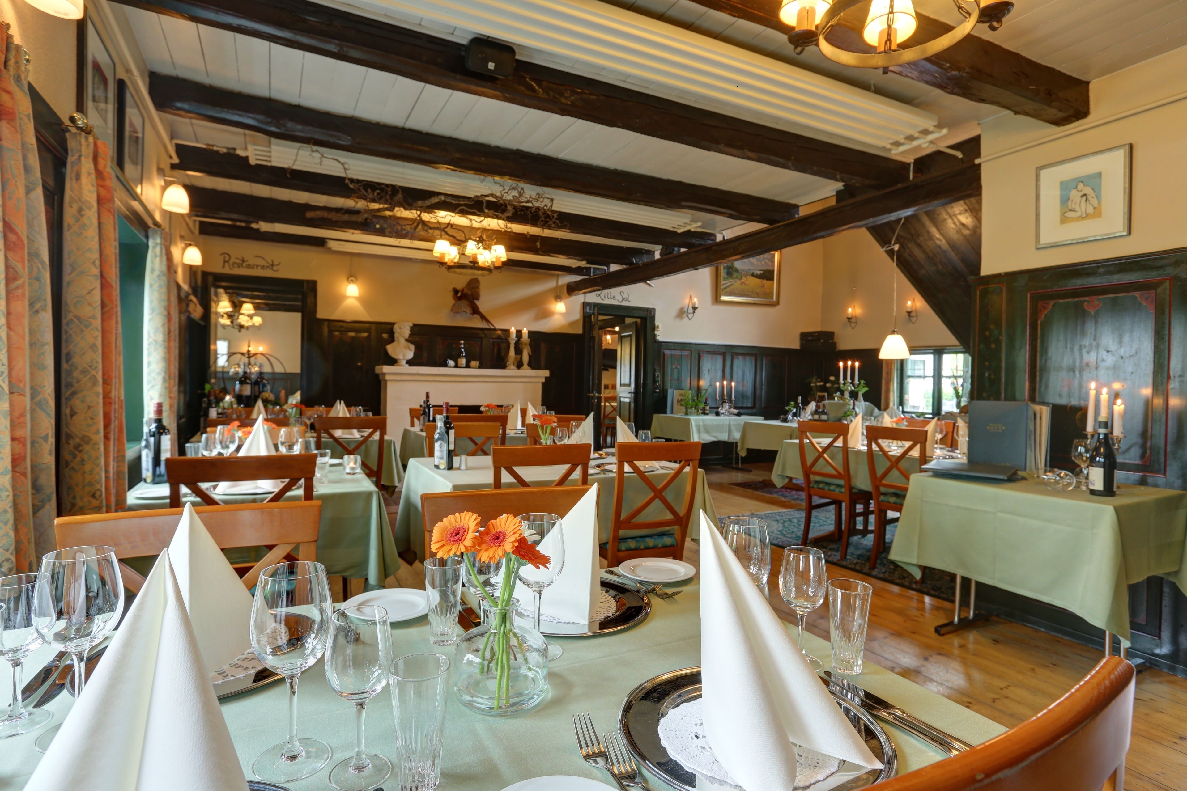 Un ristorante con travi in legno, tavoli apparecchiati per la cena e un camino.