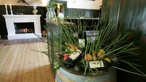 Un tonneau en bois rempli de bouteilles de vin, de fruits et de verdure, dans une pièce dotée d’une cheminée et d’un plancher en bois.