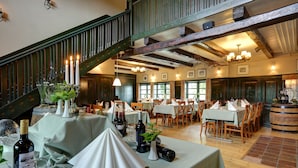 Un restaurant avec de nombreuses tables dressées, des poutres en bois au plafond et un escalier doté d’une rampe verte.