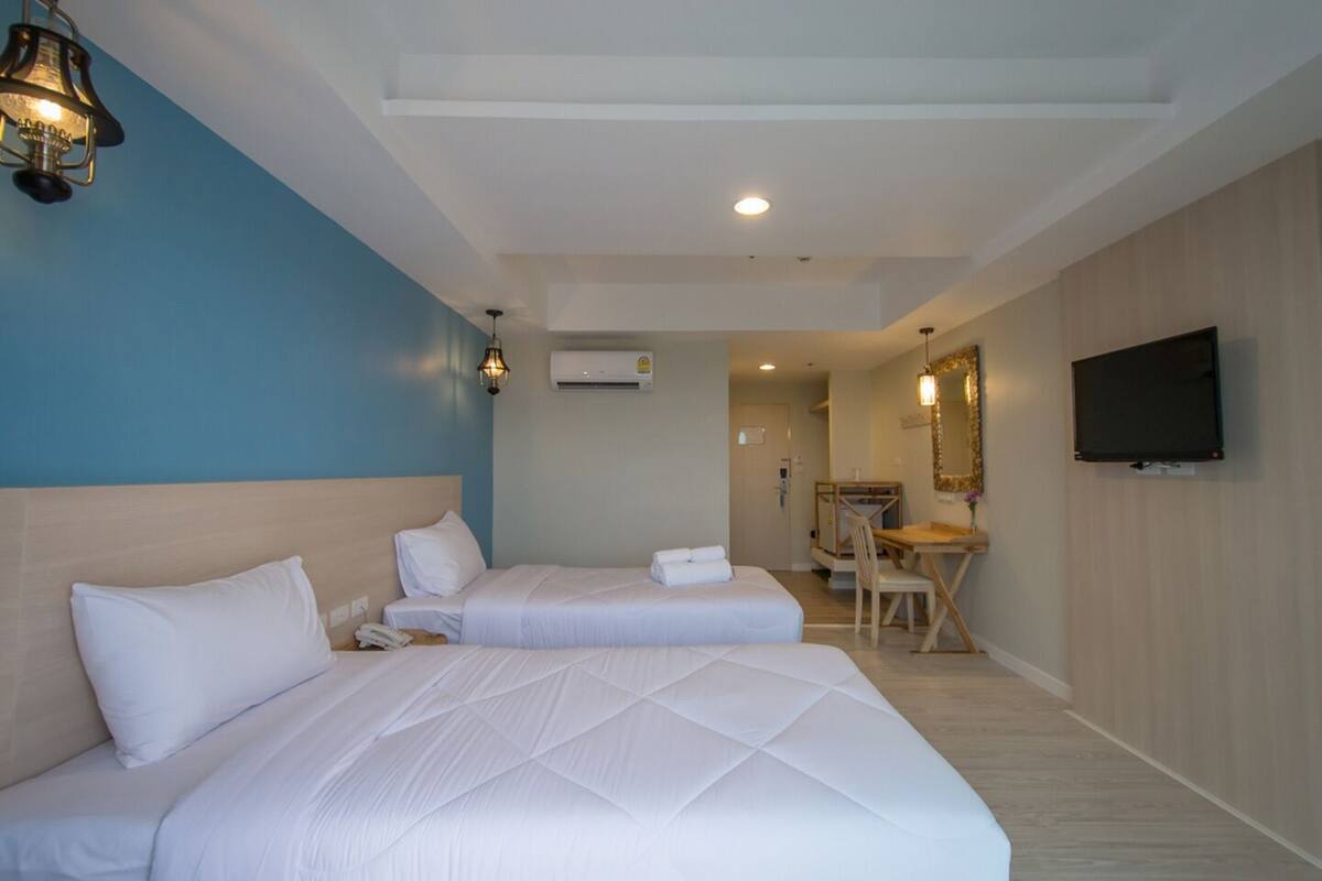 Une chambre d’hôtel avec deux lits, un bureau, une chaise, une télévision et un appareil de climatisation.
