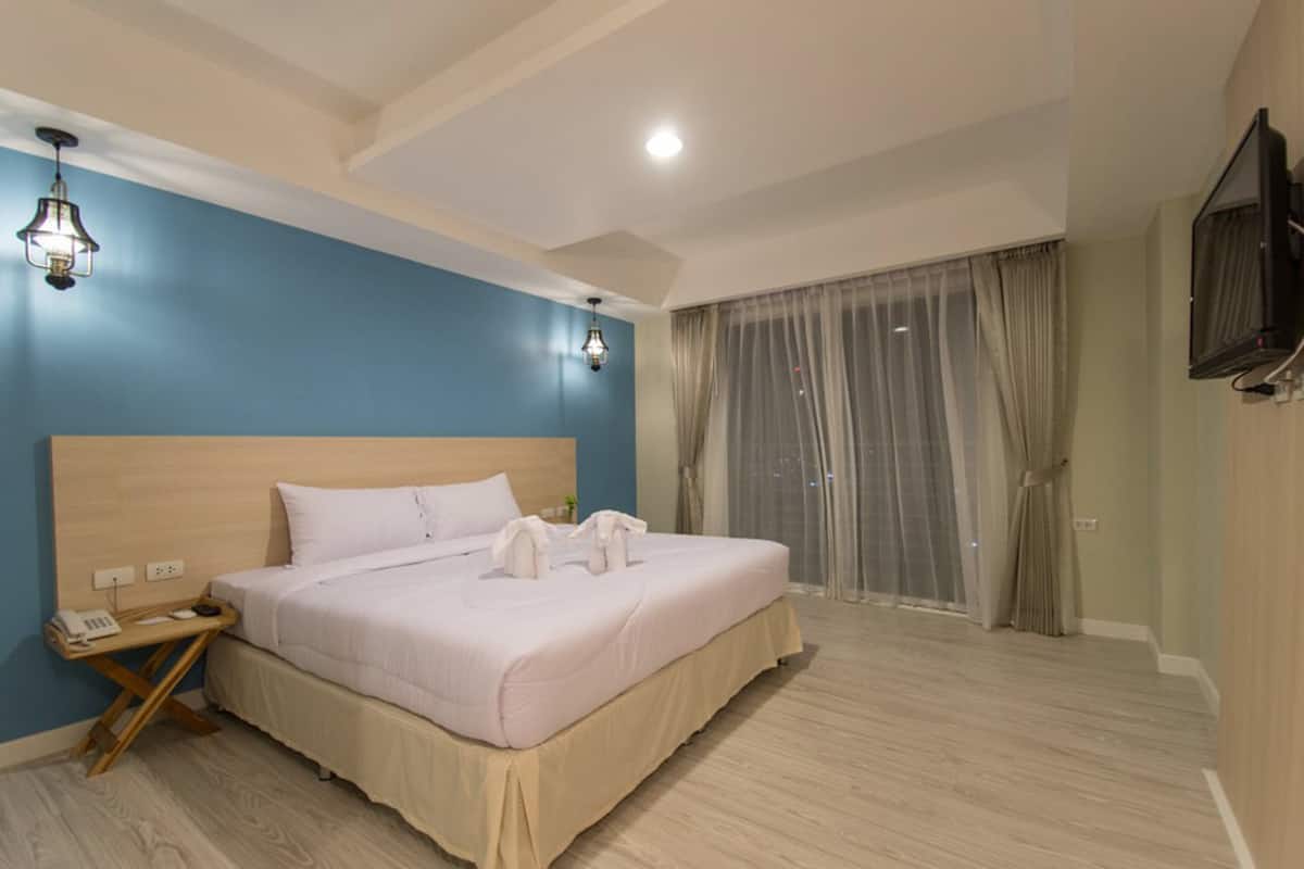Une chambre d’hôtel avec un grand lit, une tête de lit en bois, une table de chevet avec un téléphone et un téléviseur fixé au mur.
