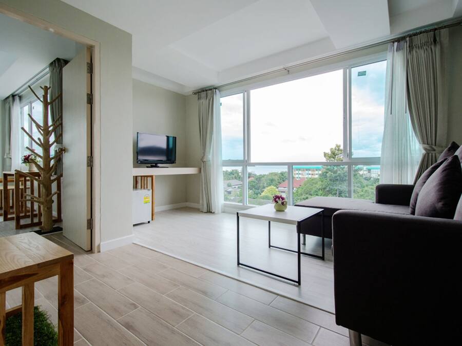 A modern living room with a large window, a flat-screen TV, a sofa, and a dining table.