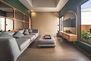 A modern living room with a grey sofa, a small ottoman, and a wooden console table with a mirror. - Ini Vie Villa Seminyak by Ini Vie Hospitality (Legian)