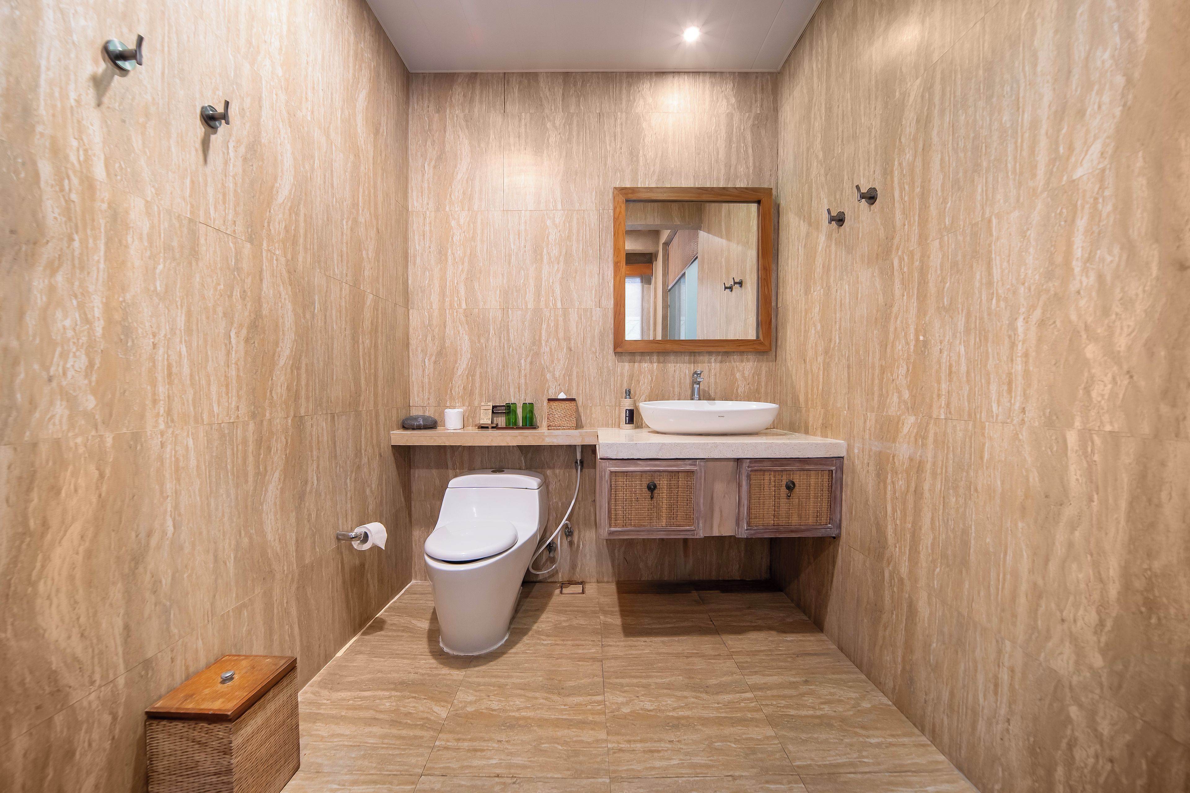 A bathroom with a toilet, sink, mirror, and a wooden cabinet.