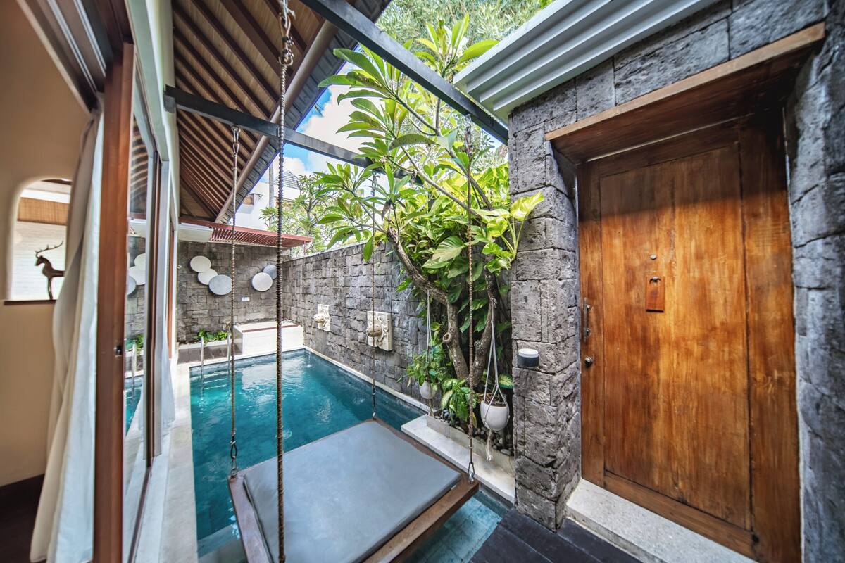 A private pool area with a swing chair, stone walls, and a wooden door.
