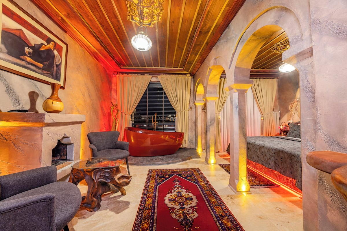 A luxurious room with a red bathtub, a fireplace, and a large rug.