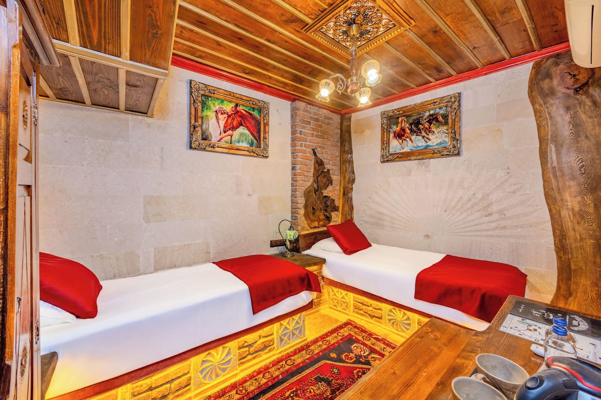 A room with two beds, wooden ceiling beams, a brick wall, and a large tree trunk.