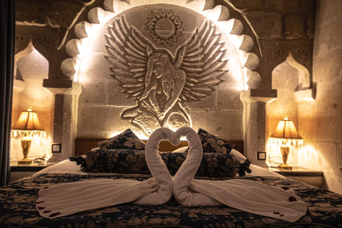A bed with a heart-shaped towel arrangement and a wall carving of an angel with wings.