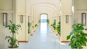 A long, white-tiled hallway with arches, lined with potted plants and framed pictures on the walls. - FLC Luxury Resort Samson (Sam Son)