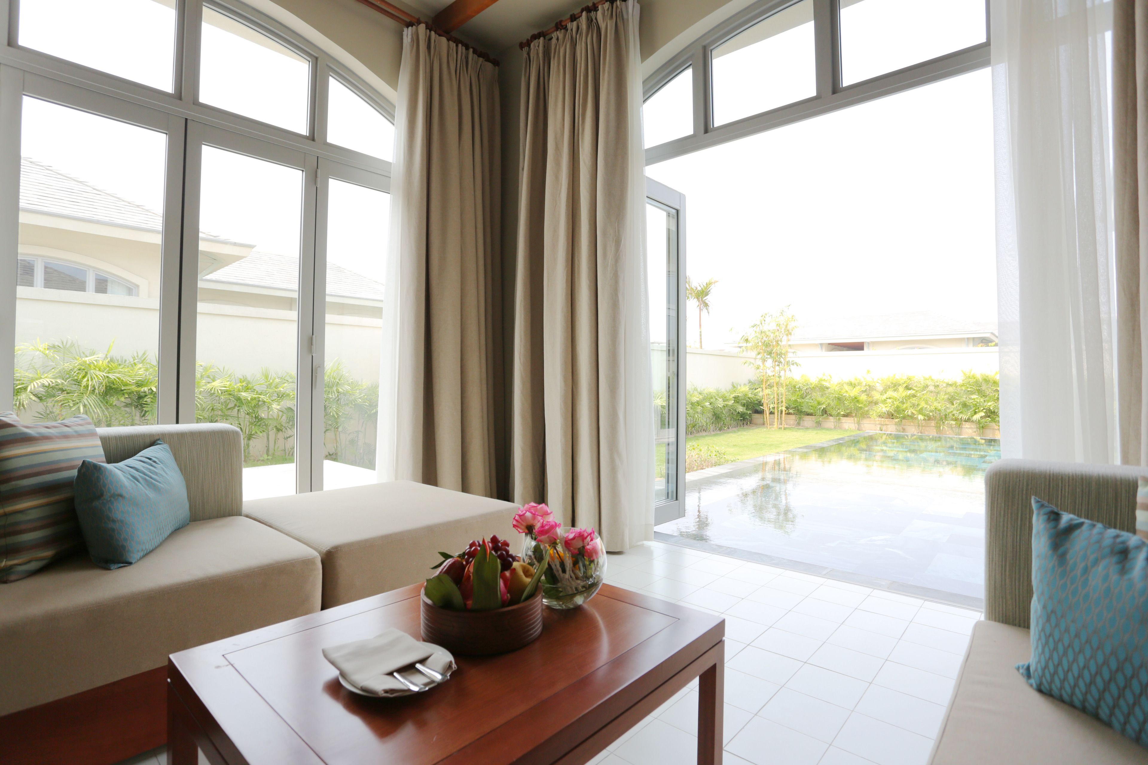 Una sala moderna con un sofá, una mesa de centro con un jarrón de flores y vistas a una piscina a través de grandes ventanales.