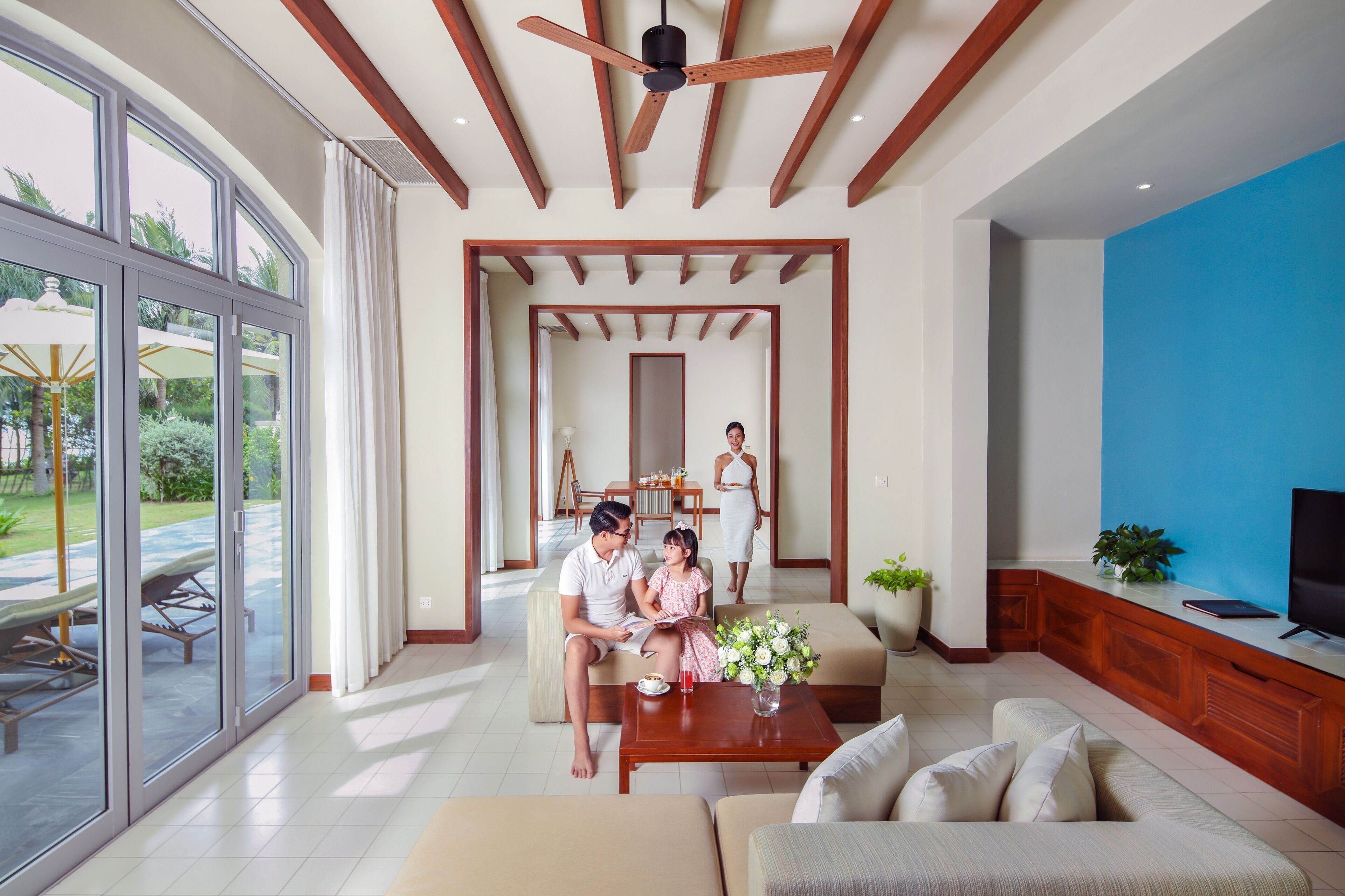 A spacious living room with a large sliding glass door leading to an outdoor area, a ceiling fan, and a television on a wooden cabinet.