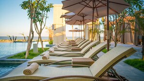 A row of sun loungers with towels, near a poolside area with umbrellas and trees. - FLC Luxury Resort Samson (Sam Son)