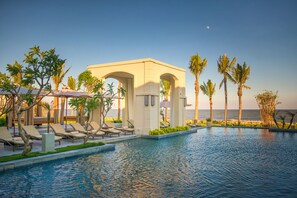 A pool area with lounge chairs and umbrellas, a covered seating area, palm trees, and a view of the ocean. - FLC Luxury Resort Samson (Sam Son)