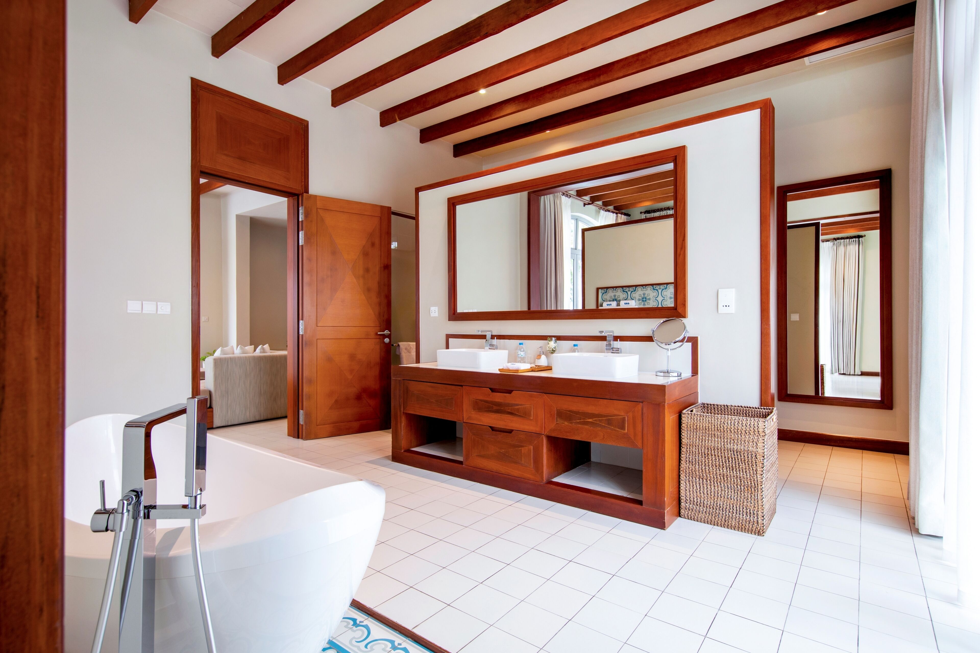 A modern bathroom with a wooden vanity, two sinks, a large mirror, and a bathtub.