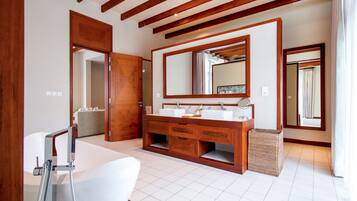 Uma casa de banho moderna com toucador de madeira, duas pias, um espelho grande e uma banheira.