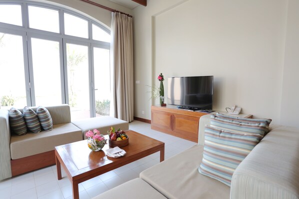 A modern living room with a sofa, a coffee table with fruit, a TV, and a large window. - FLC Luxury Resort Samson (Sam Son)