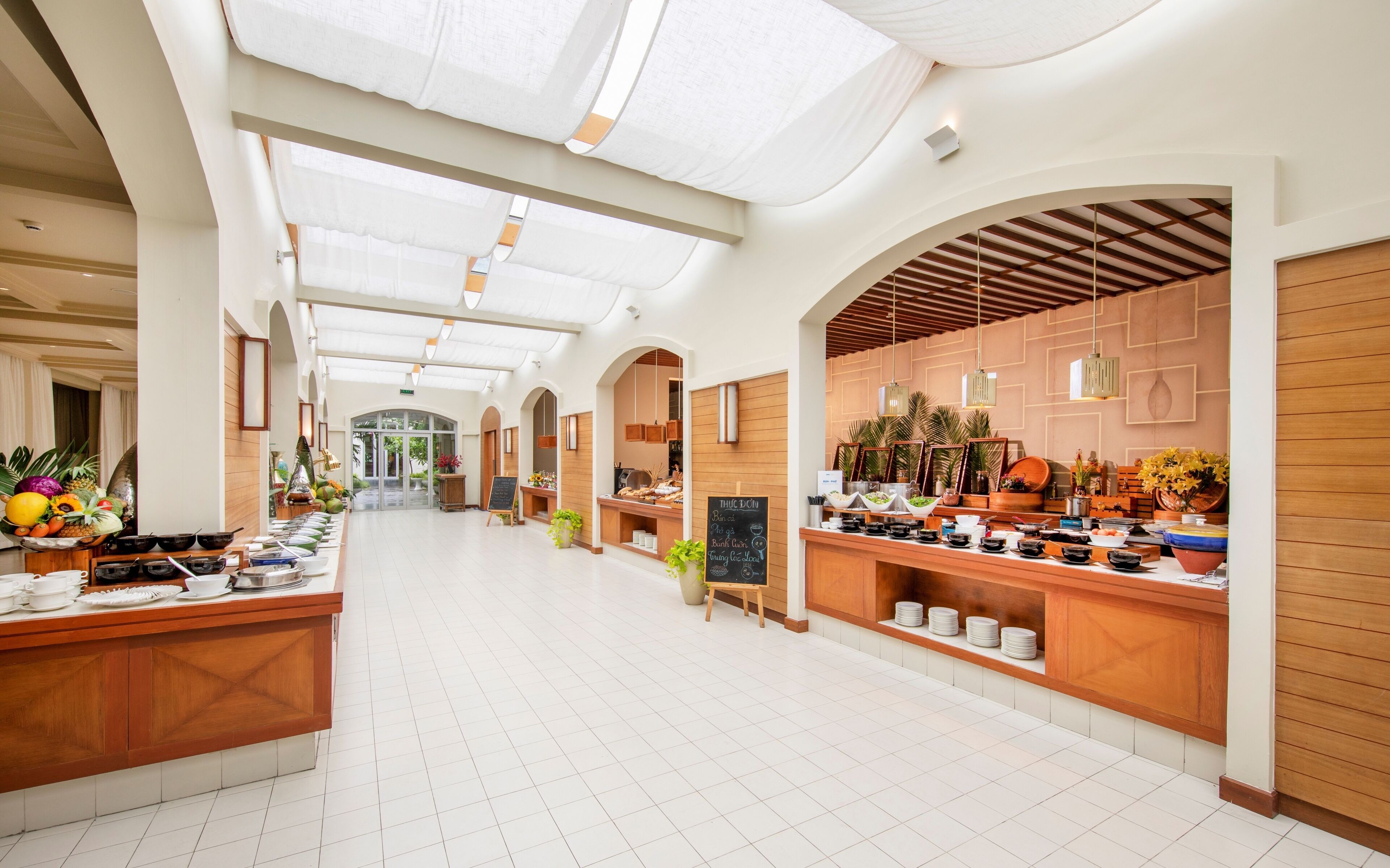 Un vaste couloir d’hôtel avec une allée centrale, des comptoirs d’accueil en bois et une porte vitrée donnant sur un espace extérieur.